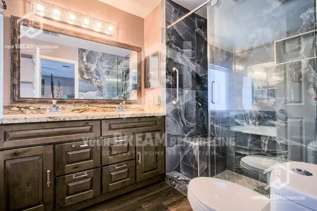 Bathroom with an espresso shaker vanity, granite top, dark marble-look shower tile and glass door