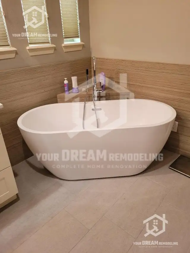 Freestanding soaking tub beside a window with a wood-look tile wainscot