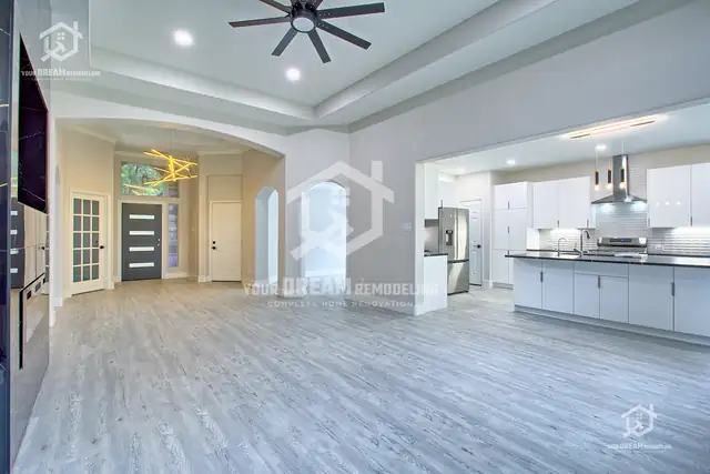 Open kitchen and living area with white cabinets, black quartz island and gray plank floors
