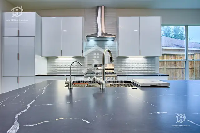 High-gloss white cabinets, glass tile backsplash and a dark quartz island with a workstation sink
