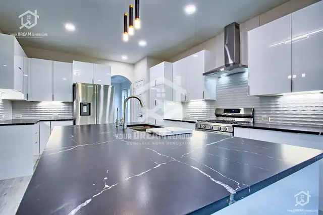 High-gloss white kitchen with a veined charcoal quartz island, stainless chimney hood and linear pendant lights