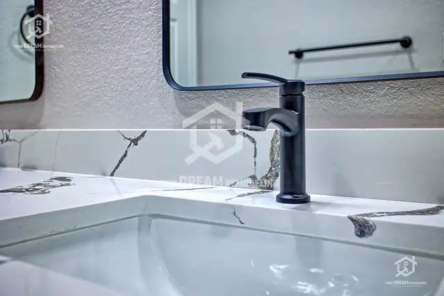 Close-up of a matte black faucet on a white quartz vanity top with dark veining and an undermount sink
