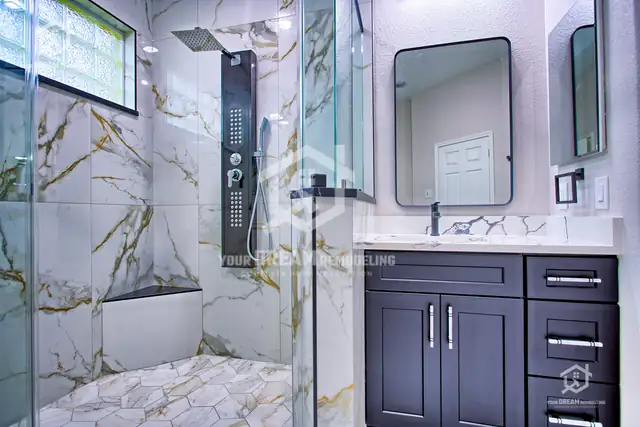 Walk-in shower with gold-veined porcelain tile, corner bench, black shower panel and frameless glass